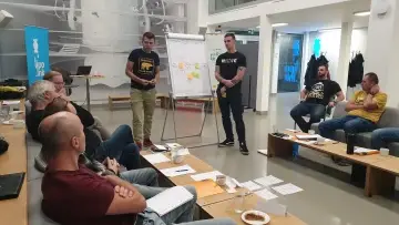 Dvojice mistrů představuje skupině svá zjištění u flipchartu